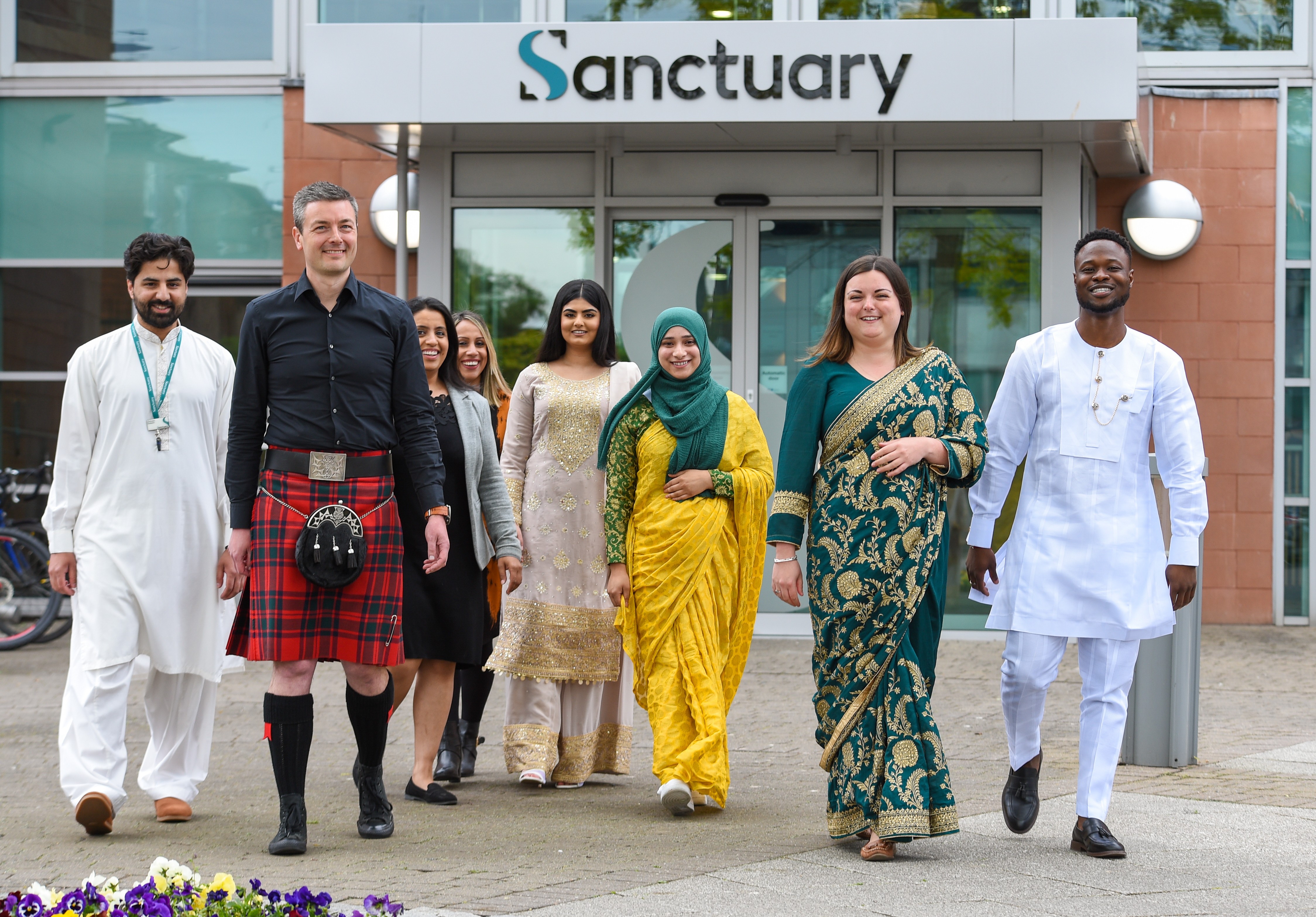 A group of 8 Sanctuary employees of different ethnicities and gender, stood outside Sanctuary Head Office, wearing their own traditional cultural clothes to celebrate cultural diversity day