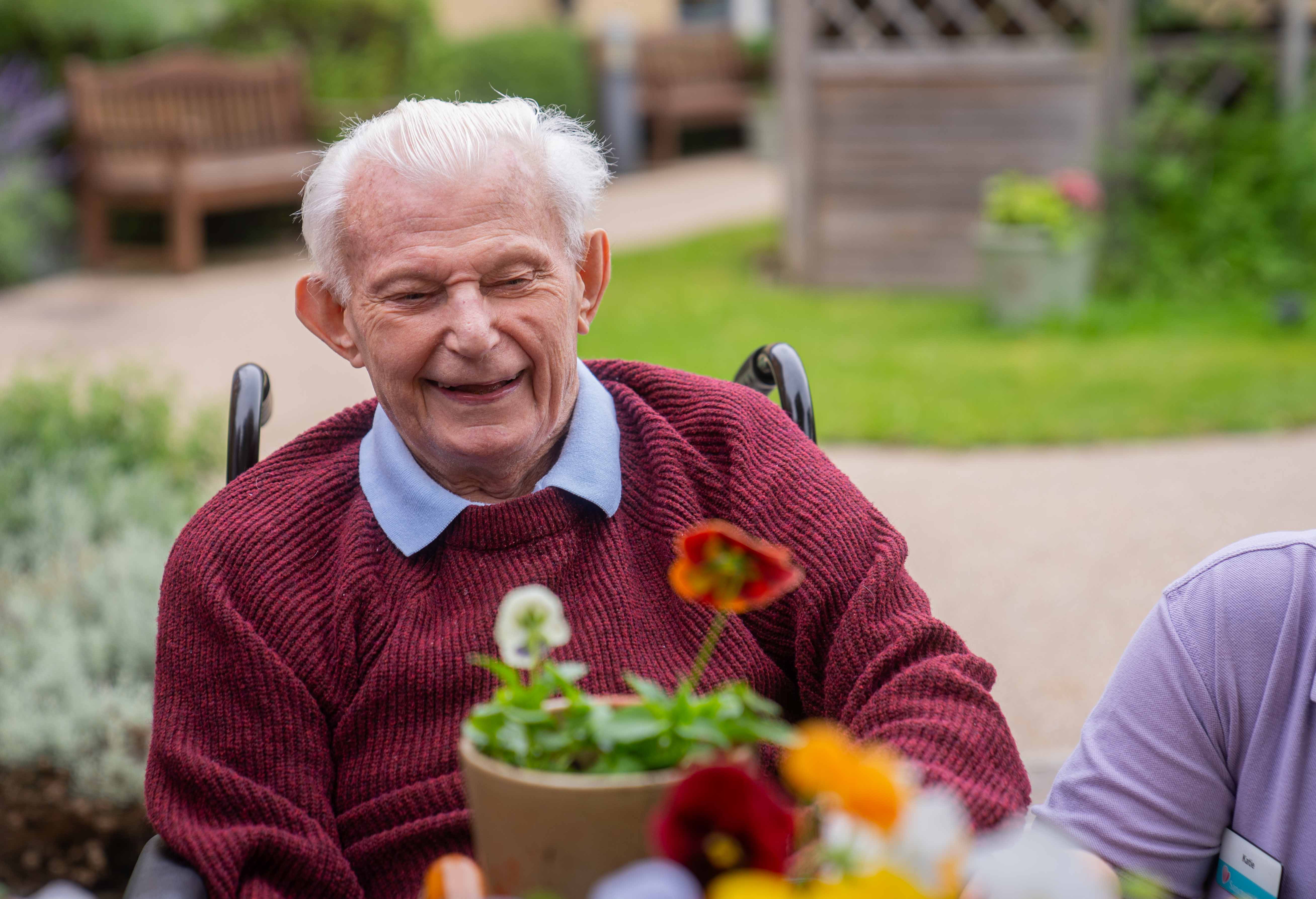 A male resident sat potting a plant and smiling in the garden