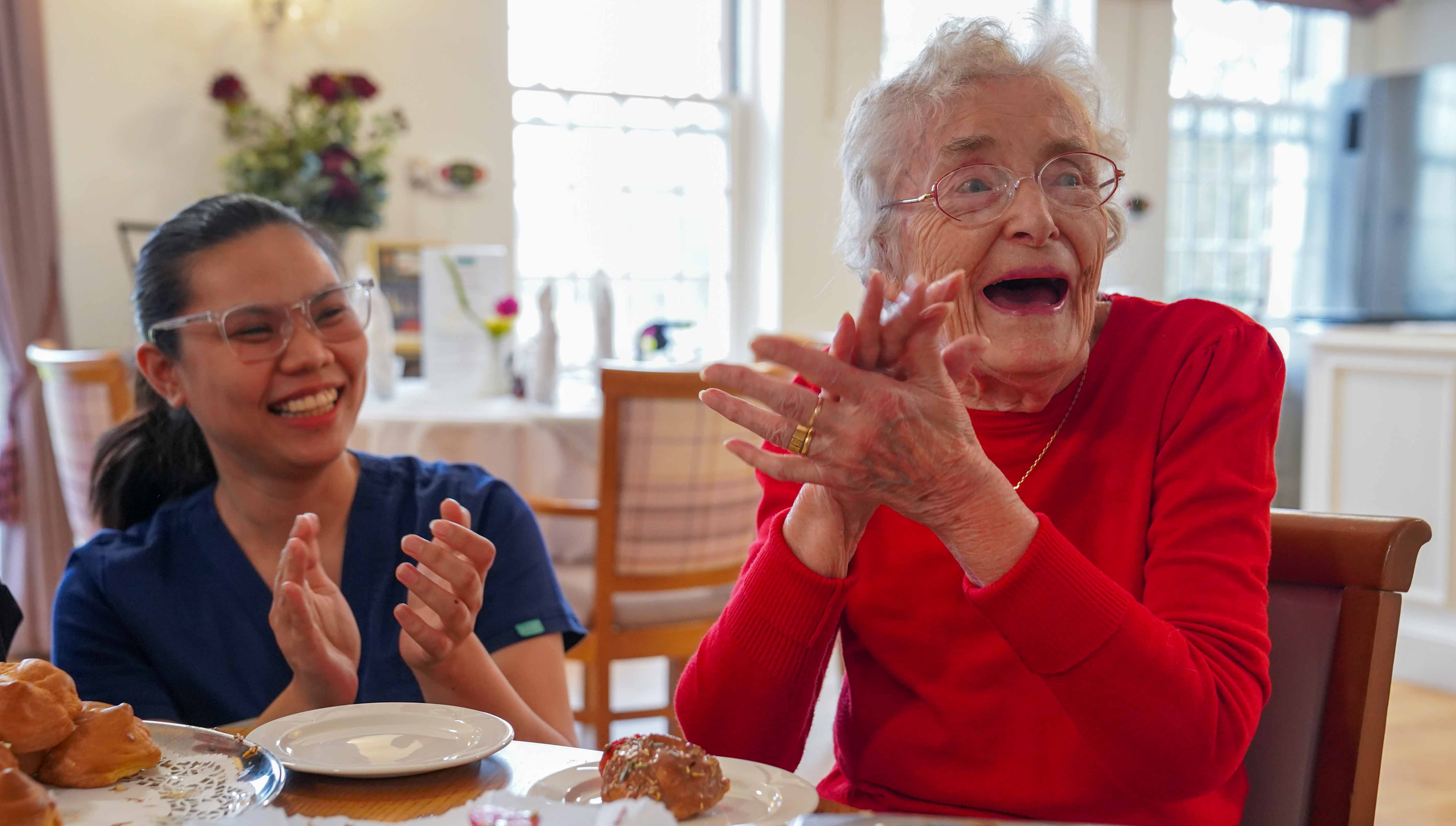 A resident and member of staff sat at a table and clapping happily