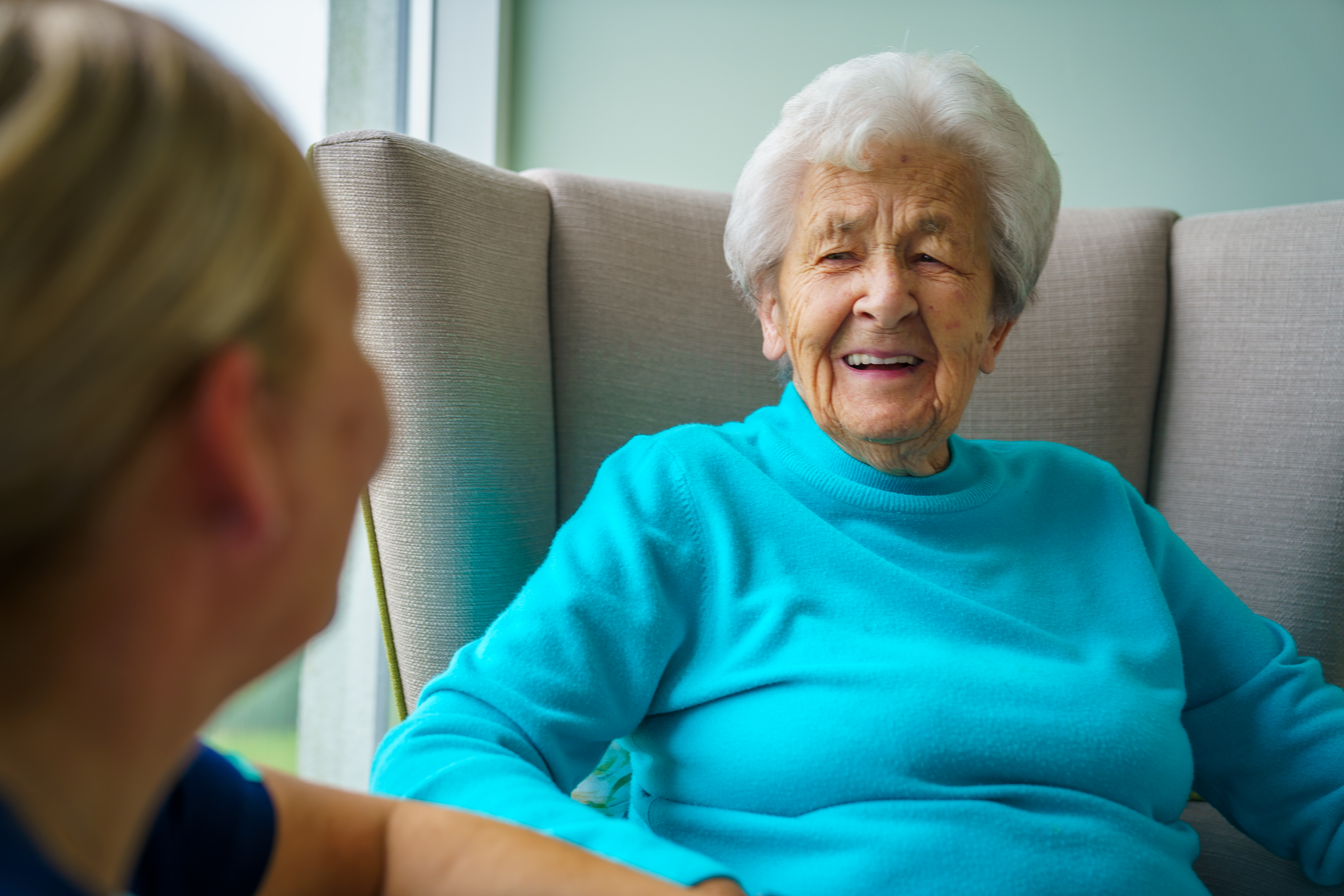 A resident sat in a comfortable armchair talking to a member of staff