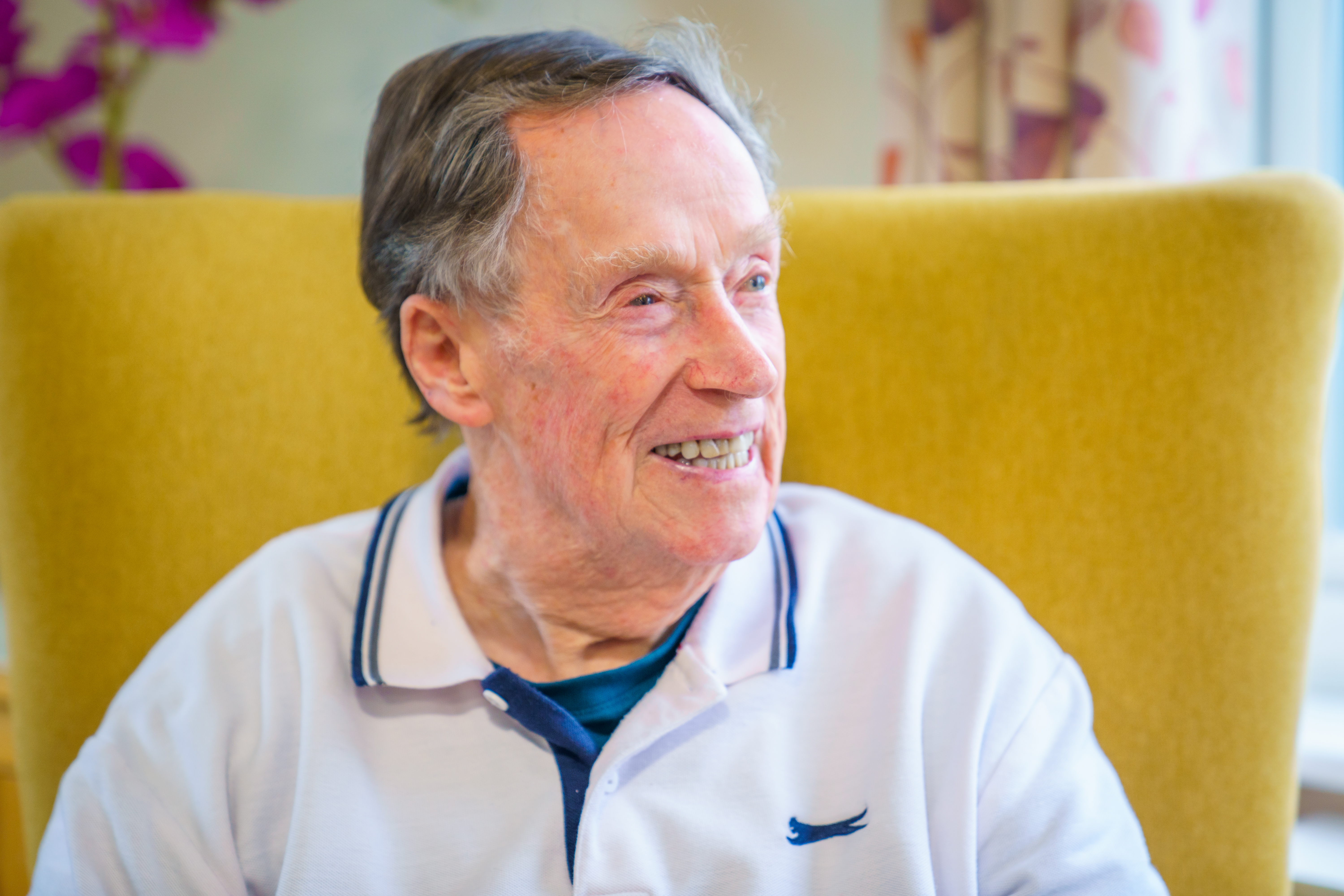 A male resident sat in a comfortable yellow armchair and smiling