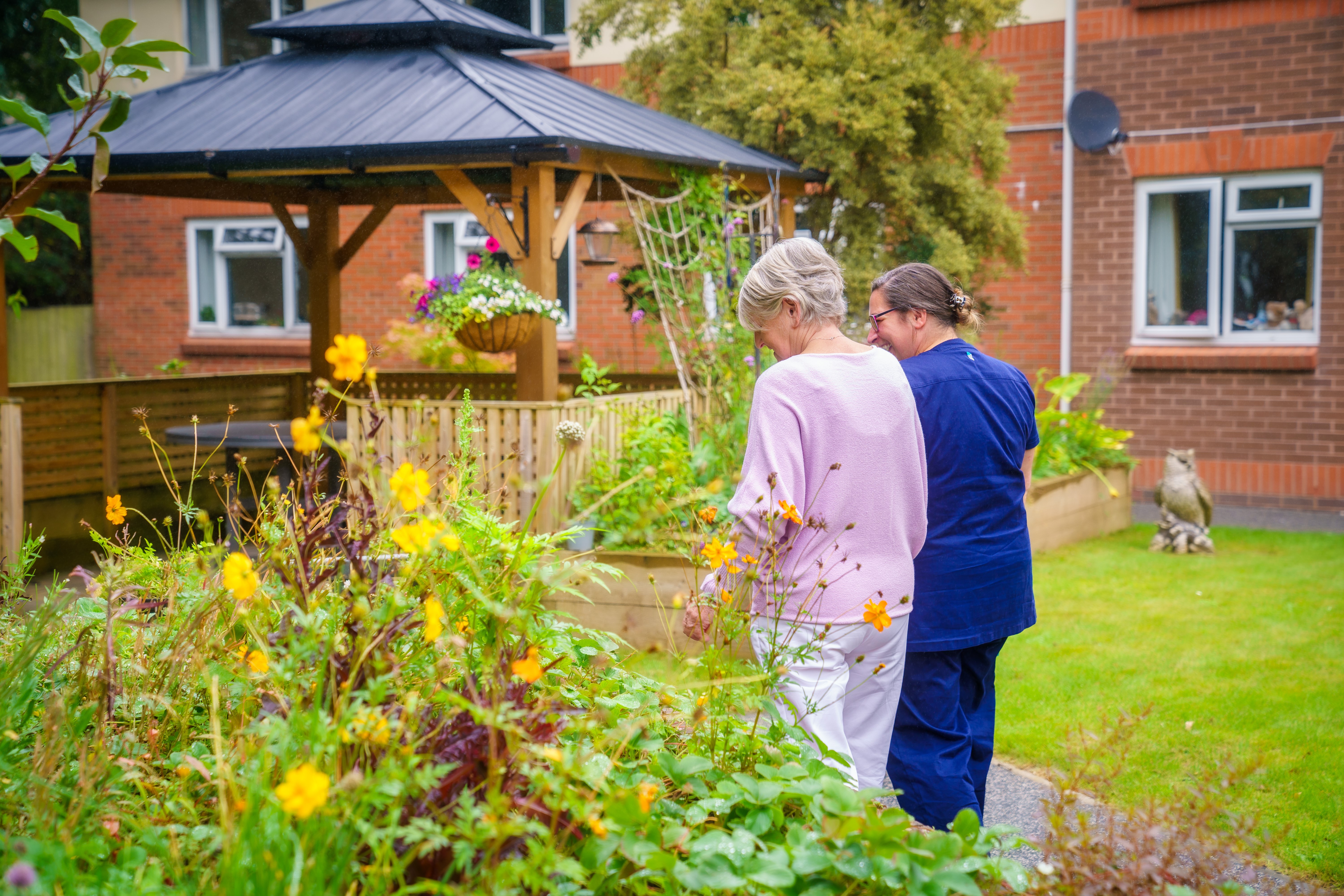 A resident and employee walking arm in arm in the garden