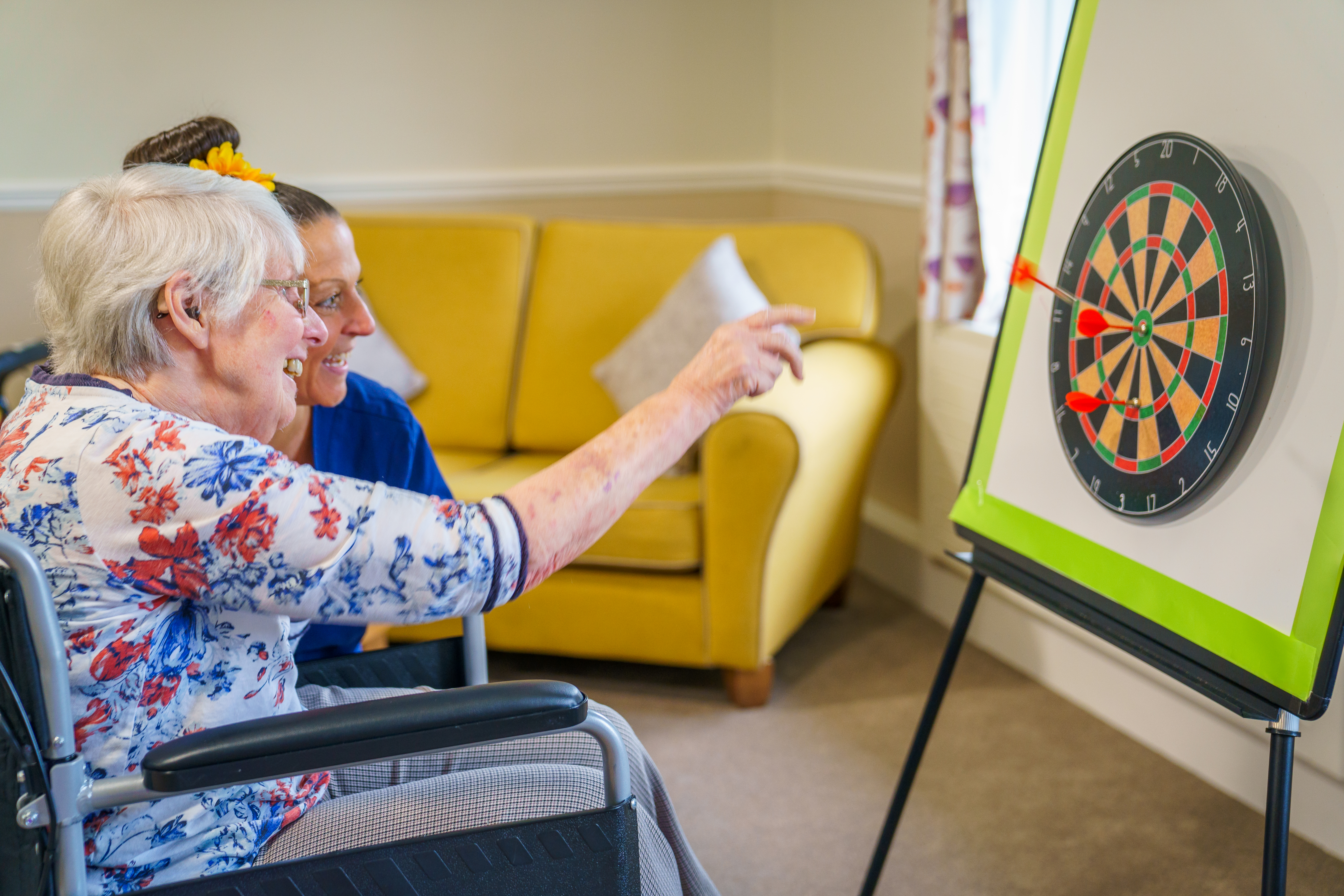 A female resident sat with a member of staff playing darts