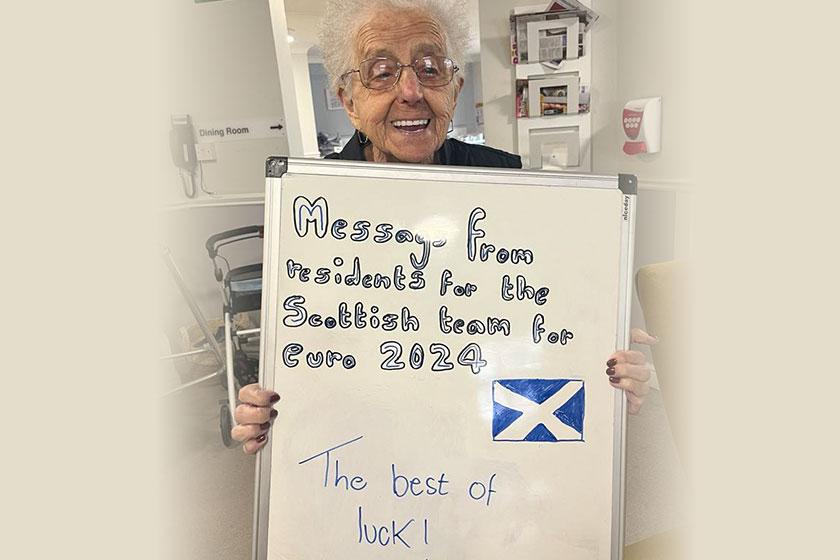 Resident Catherine Meek holding a board wishing the Scotland football team luck in their game against Germary 
