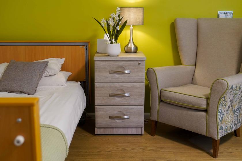 A bedroom with single bed, chest of draws and armchair next to the bed