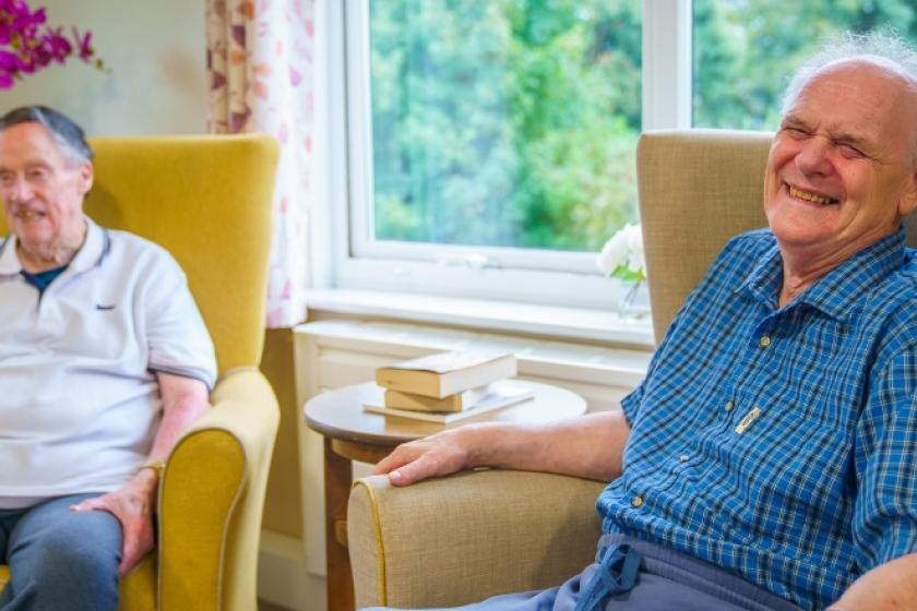 Two male residents sat next to each other on armchairs, laughing