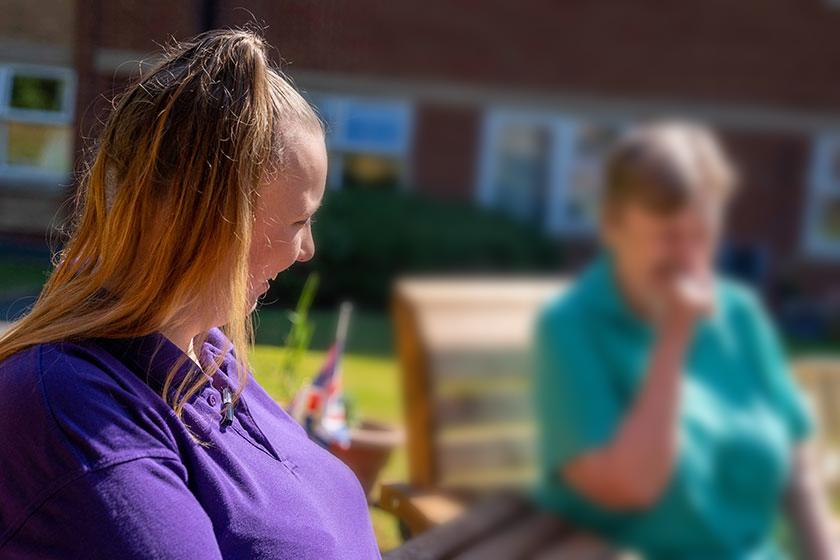 A care assistant sits outside with a resident