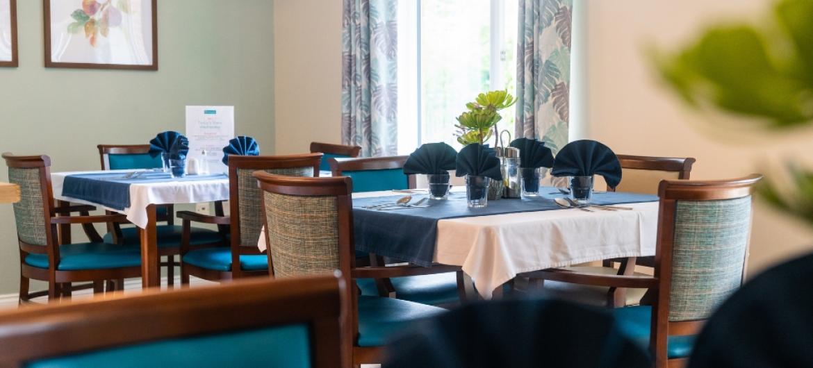 A cosy dining area with multiple tables and chairs laid out with cutlery, glasses and serviettes 
