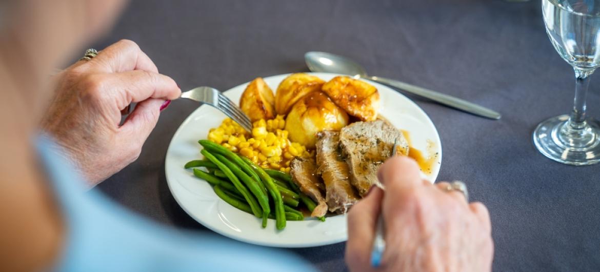 A resident eating meat, roast potatoes, sweetcorn and green beans