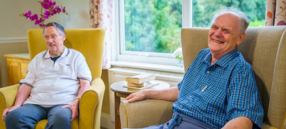 Two male residents sat next to each other on armchairs, laughing