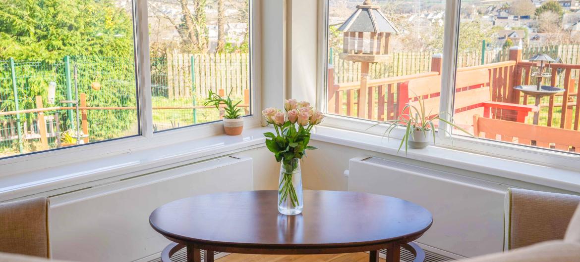 A vase holding flowers in front of two large windows looking onto a garden