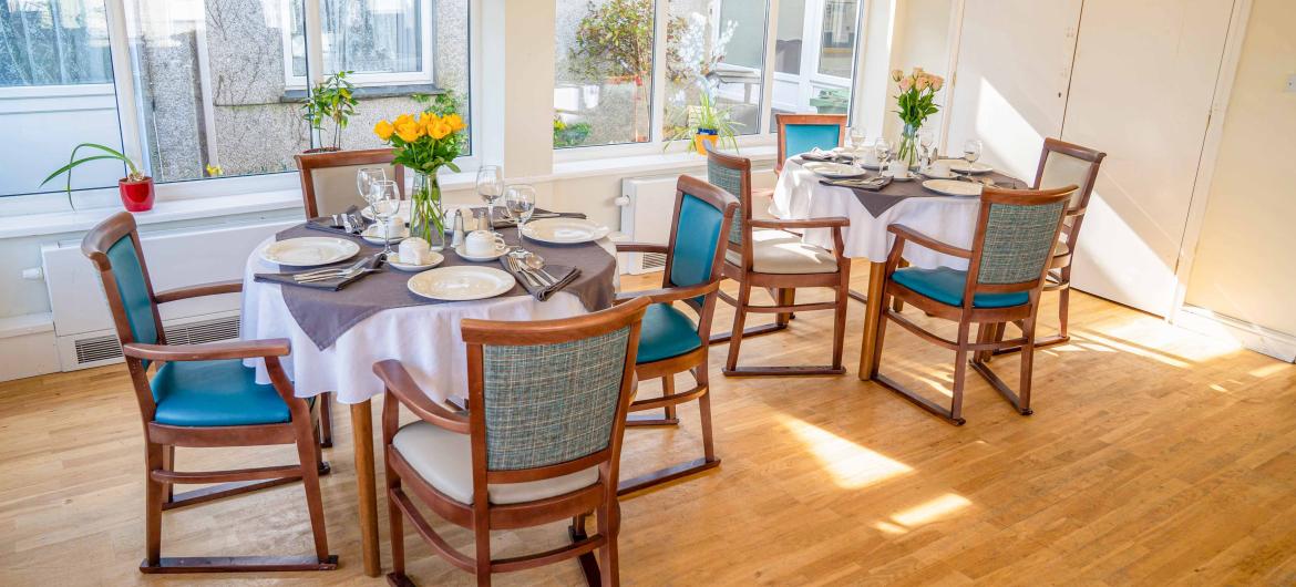 Two dining tables with dinnerware and cutlery surrounded by matching chairs