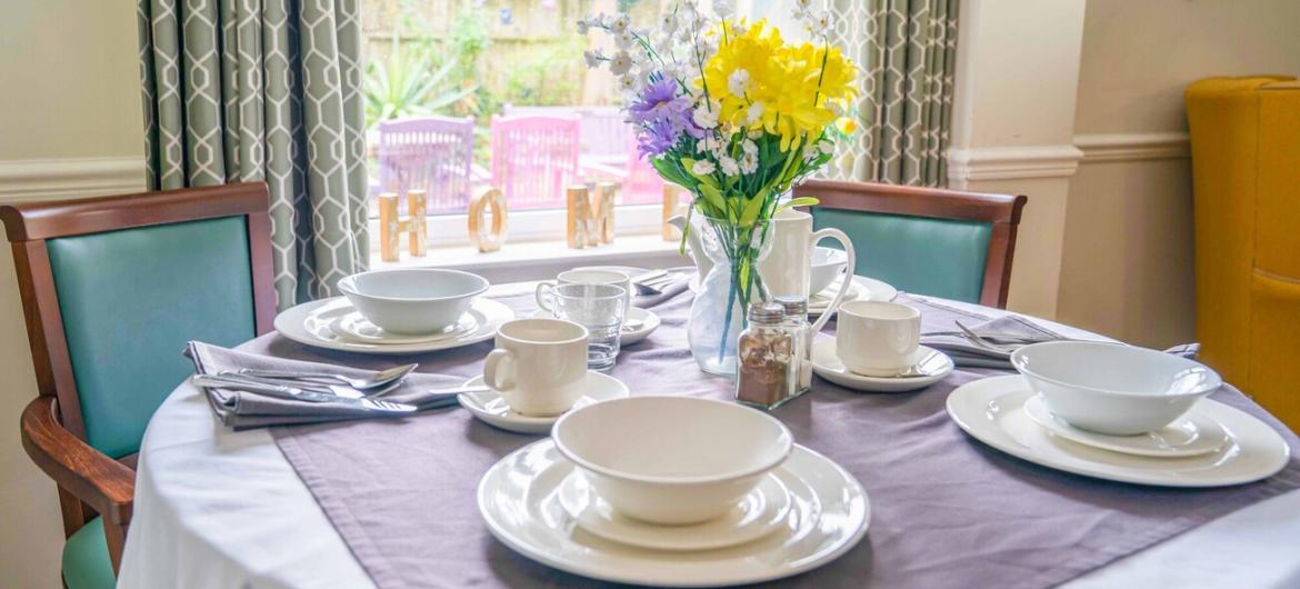 The Trevern, dining room. A bright and welcoming dining area at The Trevern with a neatly set table, cheerful flowers, and comfy chairs to feel warm, social, and homely.