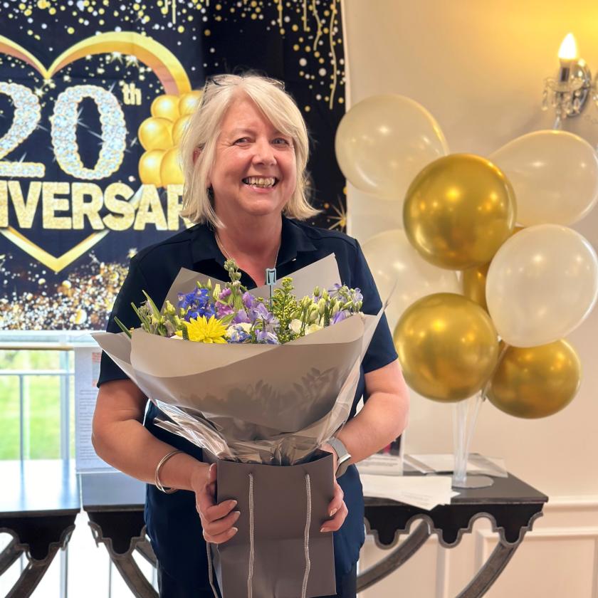 Home manager Julie smiling and holding a large bunch of flowers