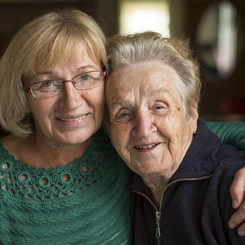 A woman stood with her arm around her elderly mother, with them both smiling