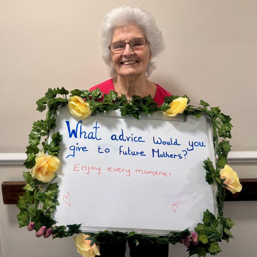 Resident Marlene holding a whiteboard with the advice to mothers saying enjoy every moment.